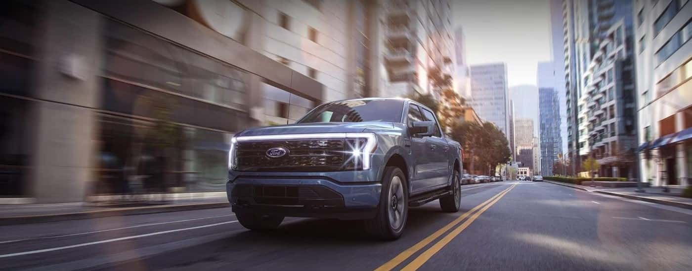 A blue 2022 Ford F-150 Lightning is shown driving to a Ford dealer near you.