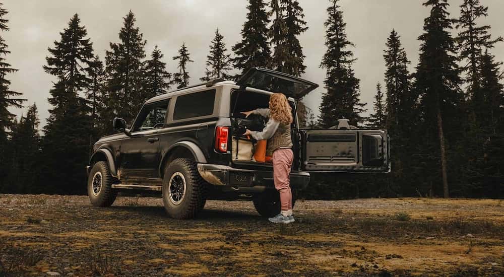 Rear view of a person loading gear into the trunk of a black 2025 Ford Bronco.