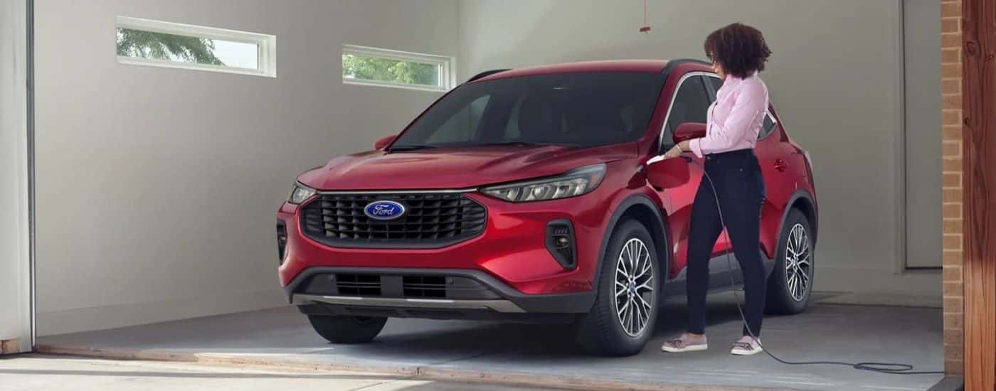 A red 2023 Ford Escape Hybrid is shown parked in a garage while charging.