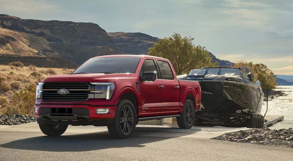 A red 2024 Ford F-150 Platinum towing a boat at a lake.