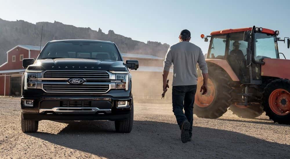 A man walking past a black 2024 Ford F-150 for sale parked next to a tractor on a farm.