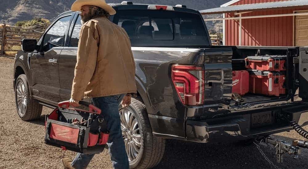 A black 2025 Ford F-150 Platinum is parked on a farm with a bed full of tools.