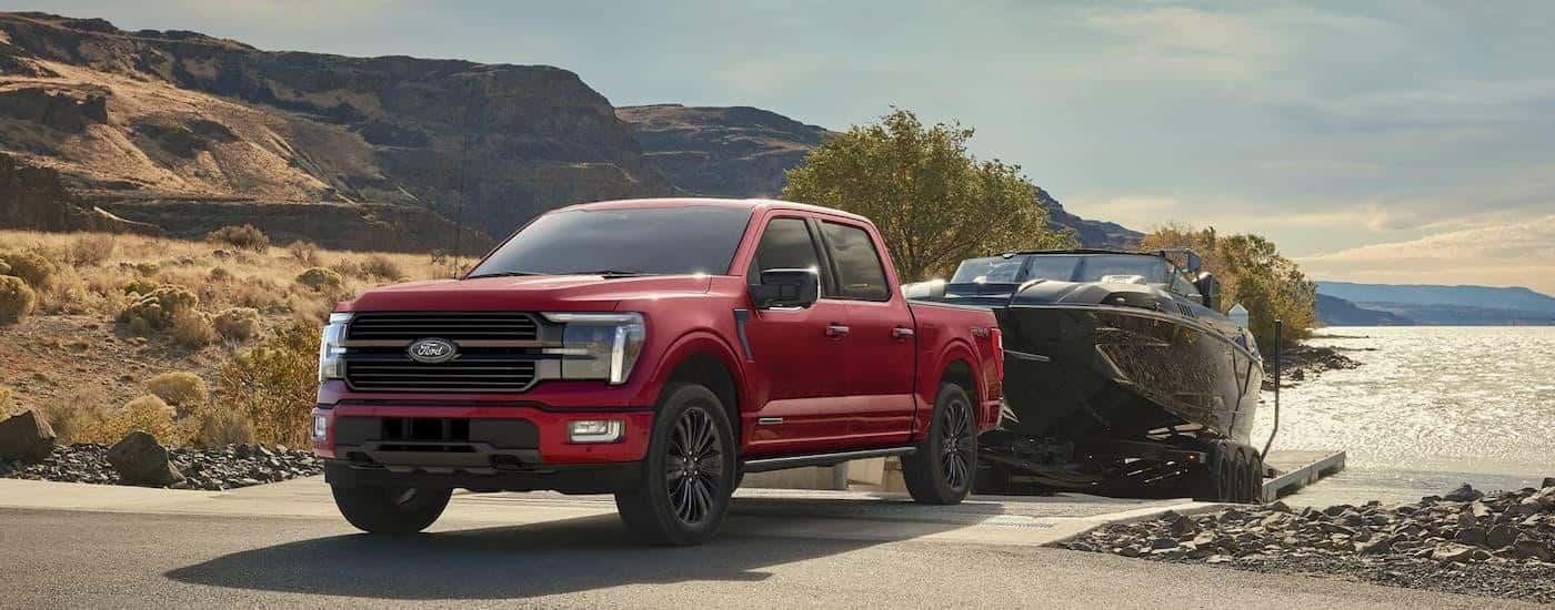 A red 2025 Ford F-150 Platinum is towing a boat out of a lake.