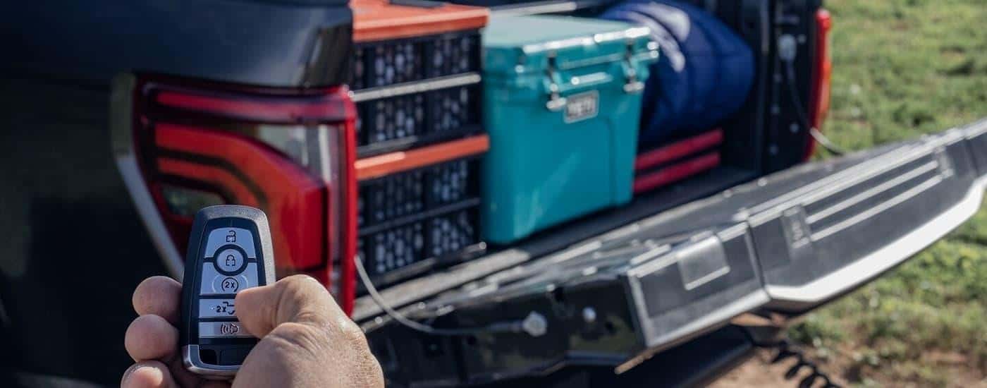 A hand is holding a keyfob next to a black 2024 Ford F-150 with supplies in the bed.