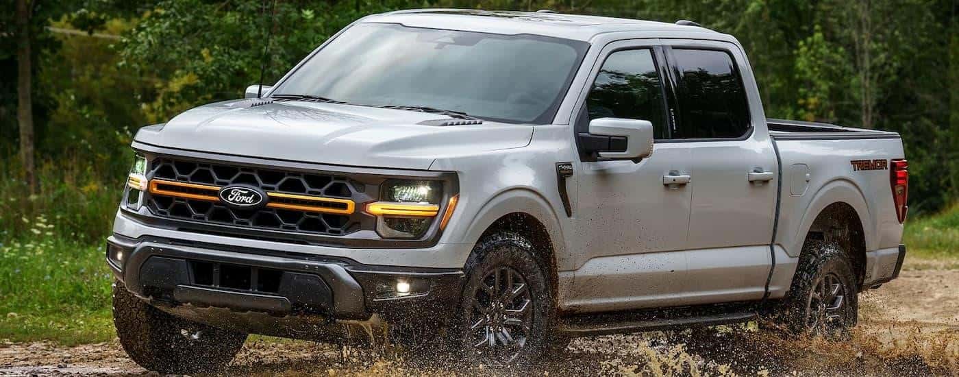 A silver 2024 Ford F-150 STX is driving on a muddy trail.