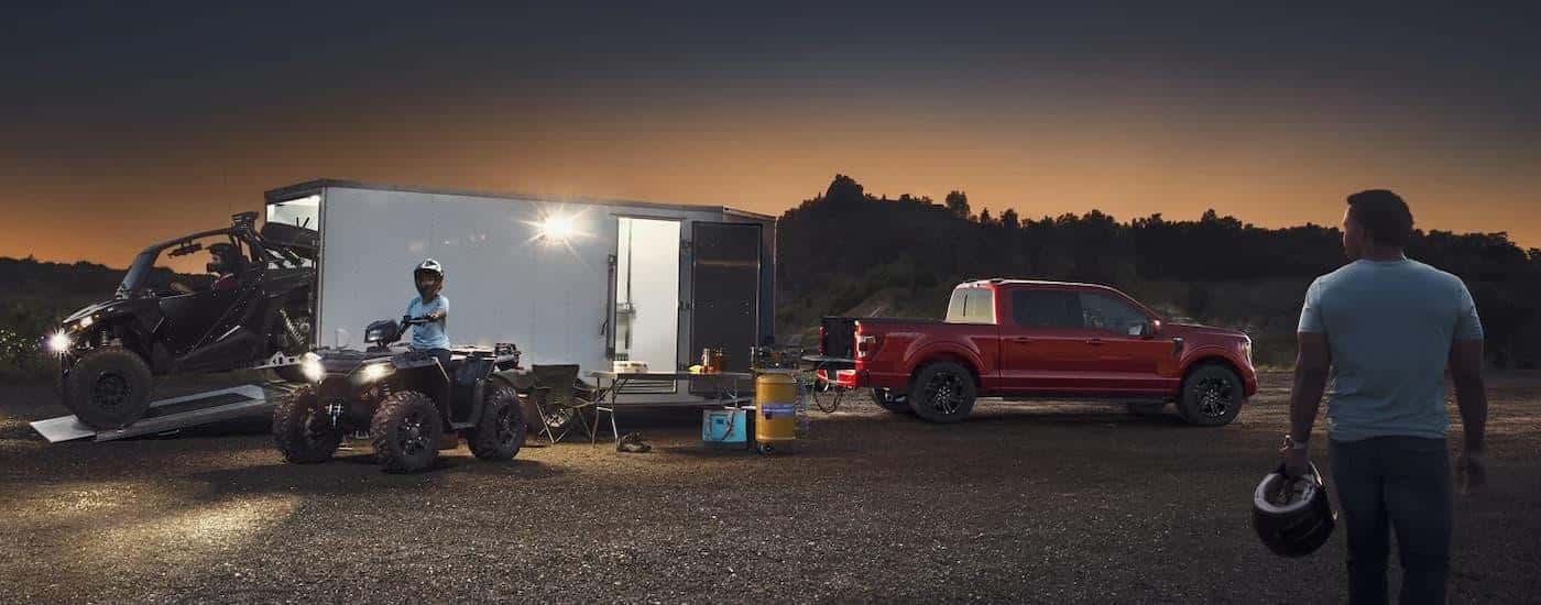 A red 2023 Ford F-150 is shown from the side towing an ATV trailer.