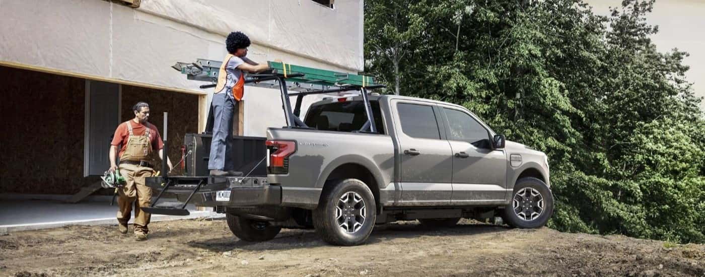 Two people are shown next to a silver 2023 Ford F-150 Lightning at a construction site.