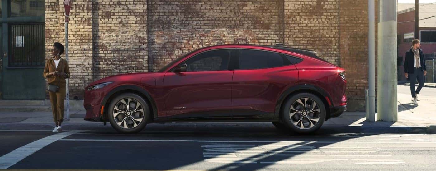 A red 2021 Ford Mustang Mach-E is shown from the side in front of a brick building after leaving a Ford Mach-E dealer.