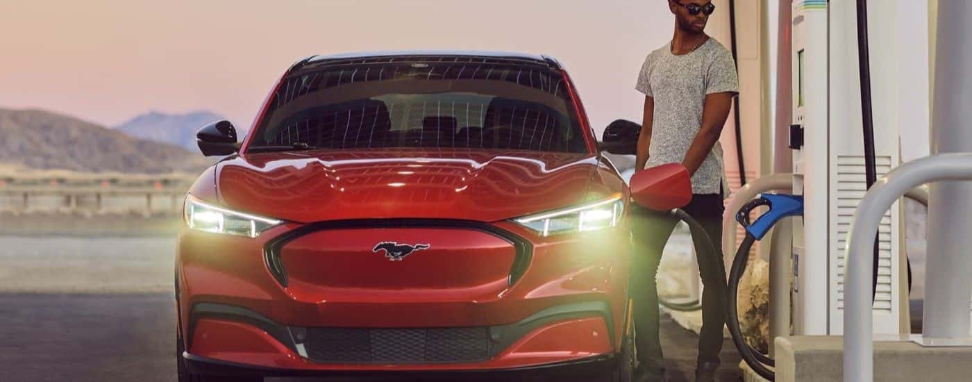 A red 2023 Ford Mustang Mach-E is shown charging at a station.