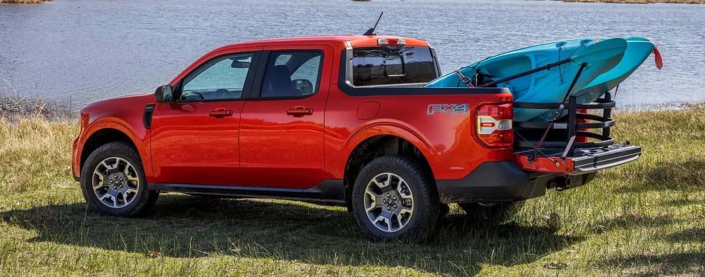 A red 2024 Ford Maverick FX4 with a kayak in the bed parked near water.