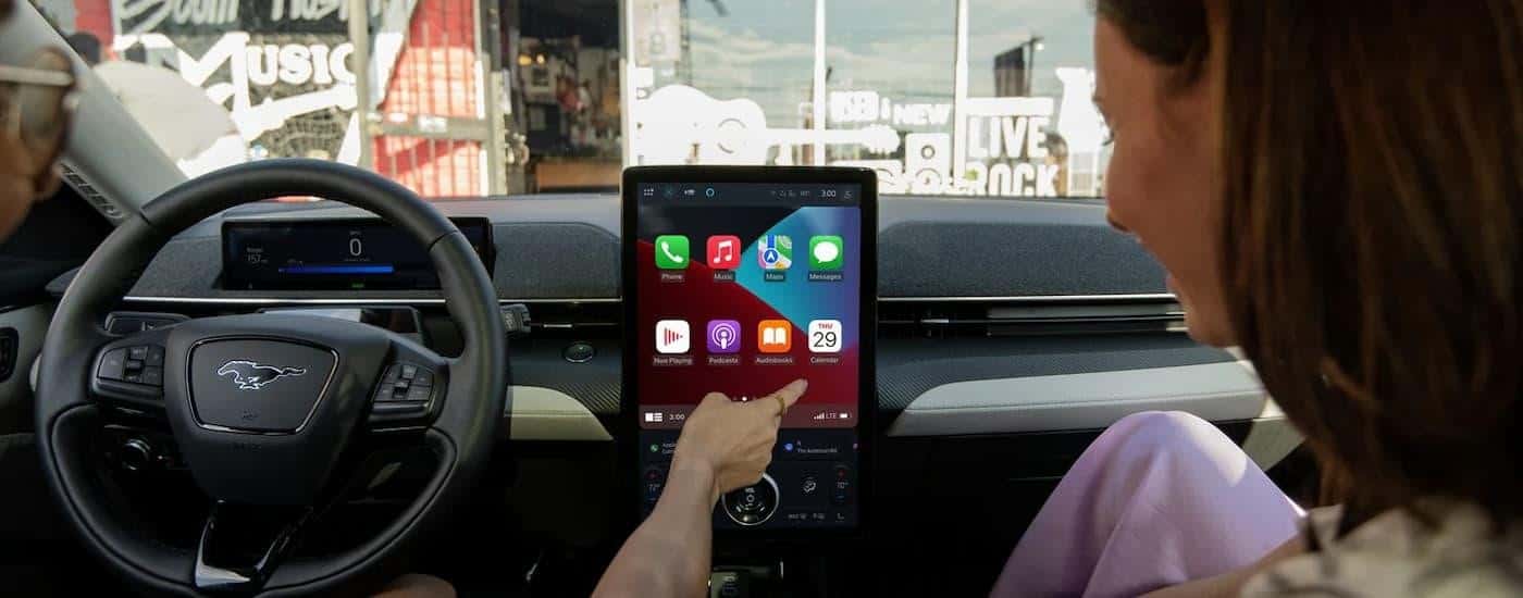 Two people are using the infotainment screen in a 2024 Ford Mustang Mach-E for sale.