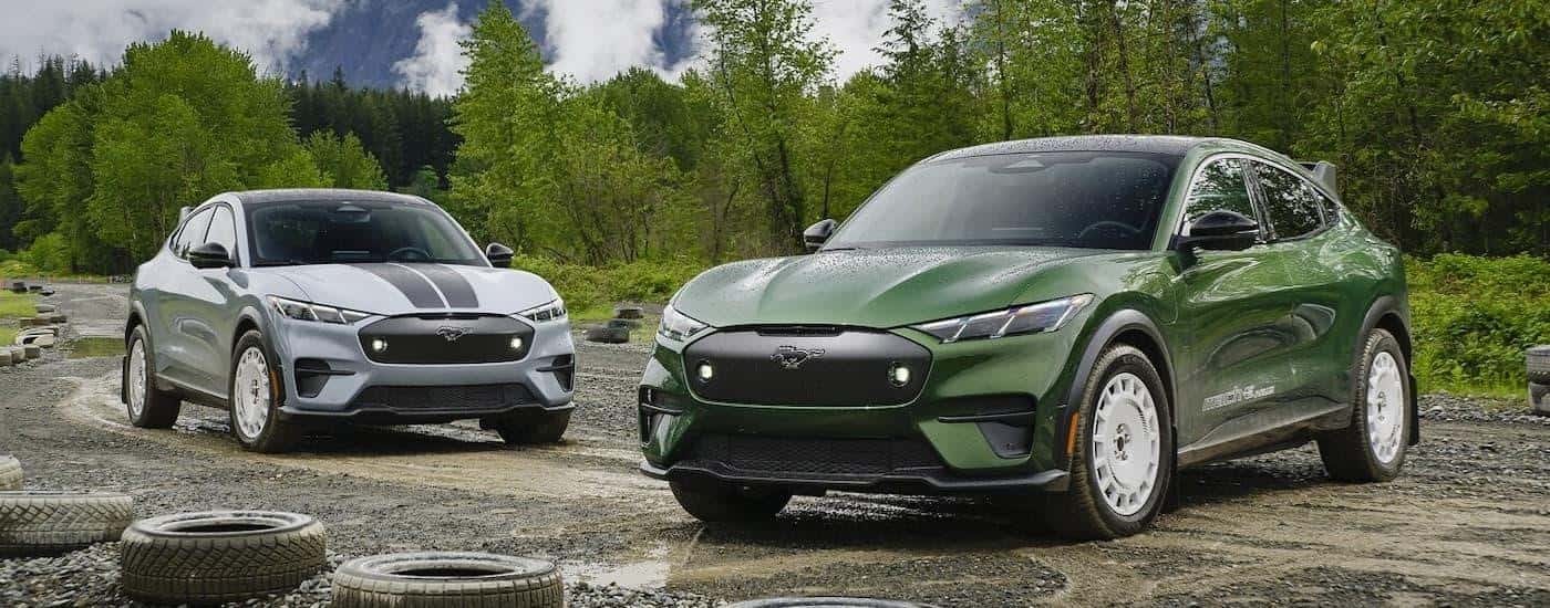 A green and a grey 2024 Ford Mustang Mach-E Rallysport are parked on a gravel track.