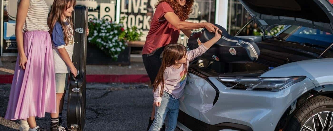 A family is putting cargo into the frunk in a blue 2024 Ford Mustang Mach-E.