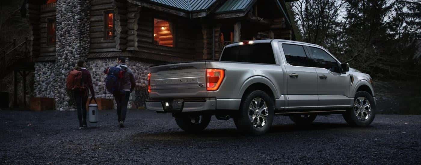 A grey 2023 Ford F-150 is shown from the side parked in front of a cabin.