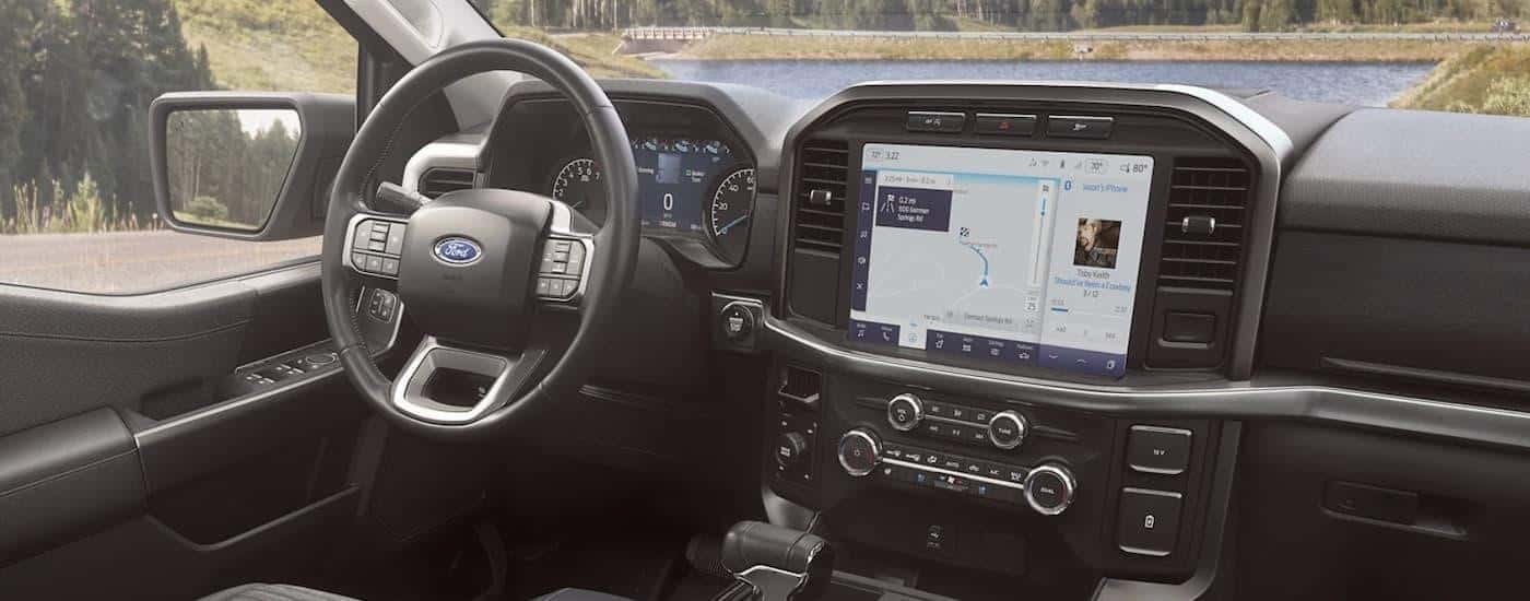 The black interior of a 2023 Ford F-150 shows the steering wheel and infotainment screen.