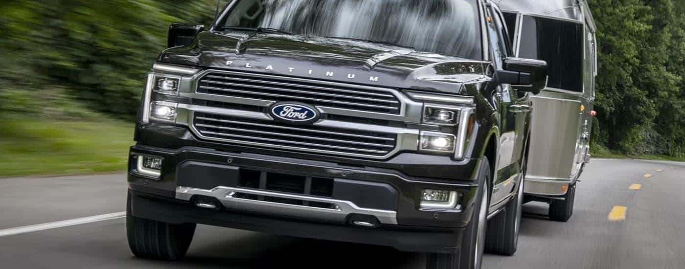 A grey 2024 Ford F-150 Platinum is towing a silver camper on a winding road.
