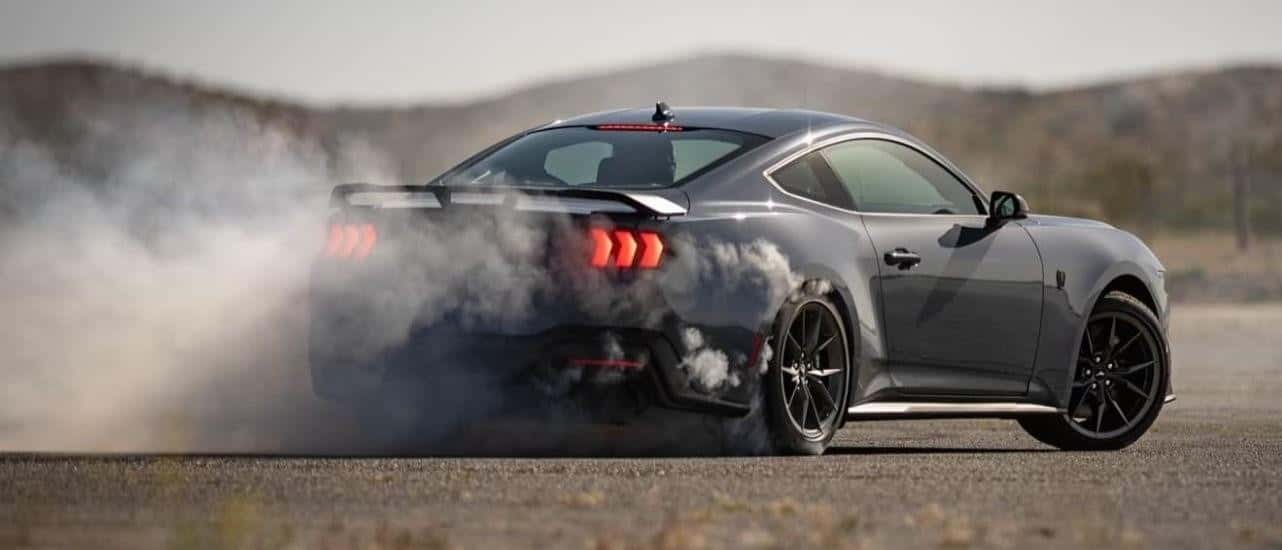 A grey 2024 Ford Mustang Dark Horse is shown from behind doing a burnout.