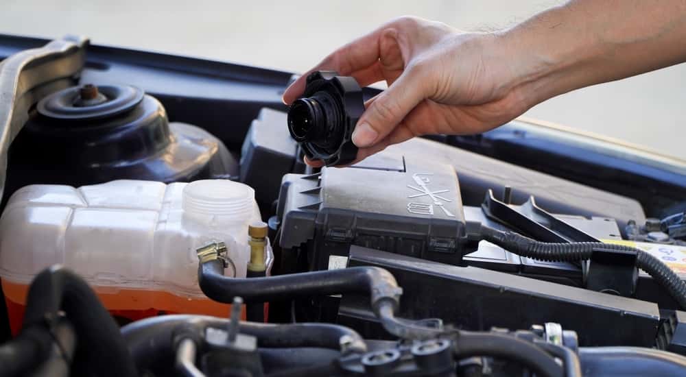 A close-up of a hand holding a radiator cap over an engine.