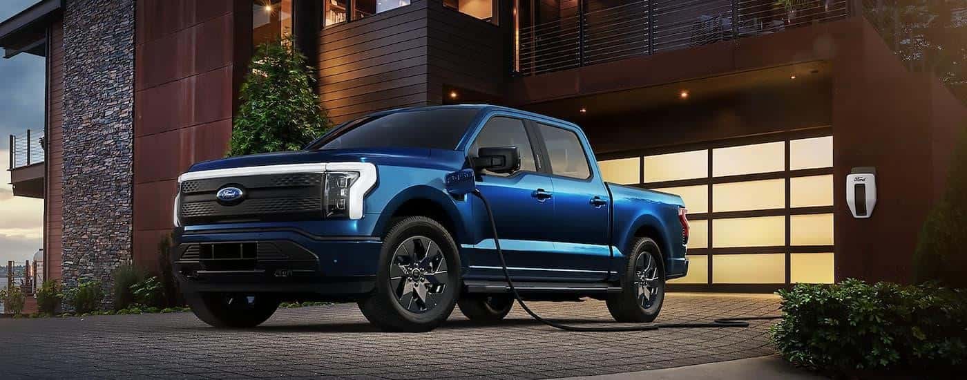 A blue 2023 Ford F-150 Lightning is shown parked on a driveway while charging.