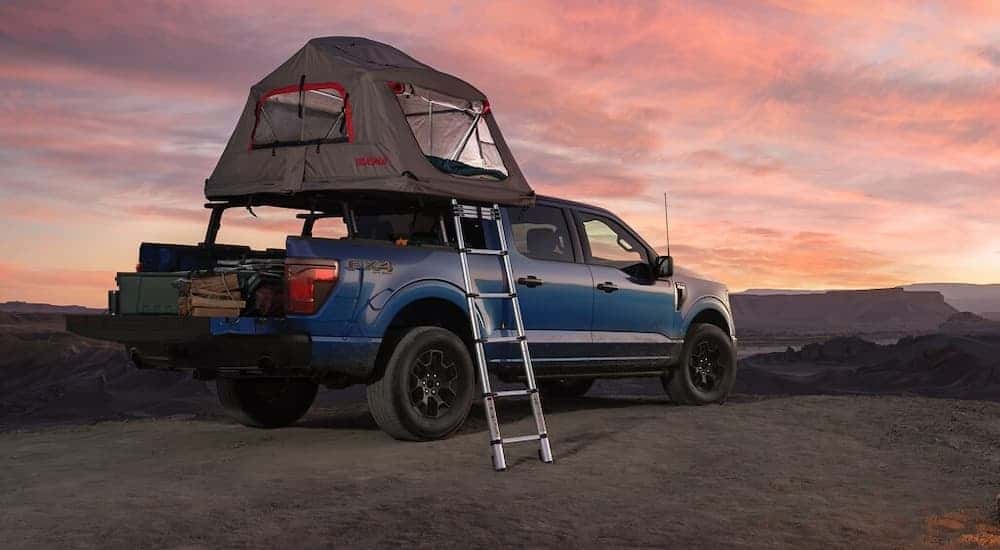 A blue 2025 Ford F-150 is parked at a remote campsite during a sunset.