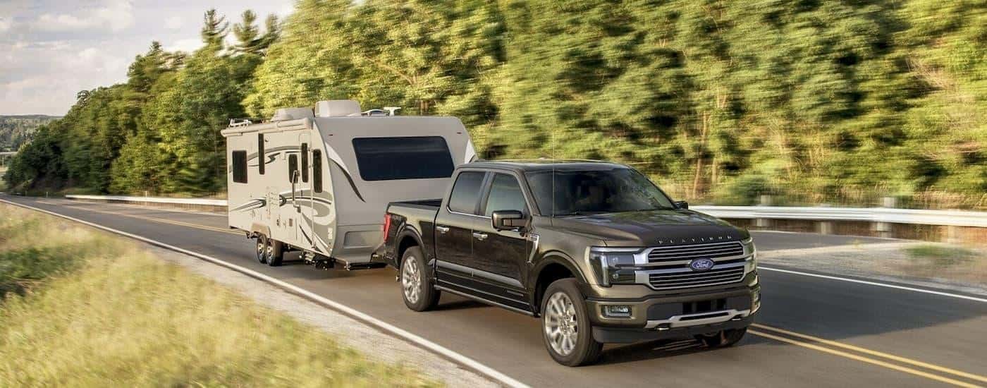 A black 2025 Ford F-150 Platinum is towing a camper on an open road.
