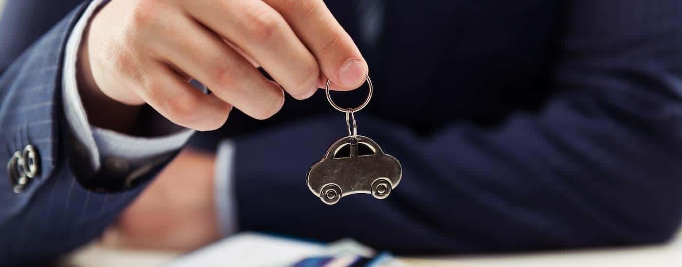 A salesman is holding up a small silver keychain shaped like a car.