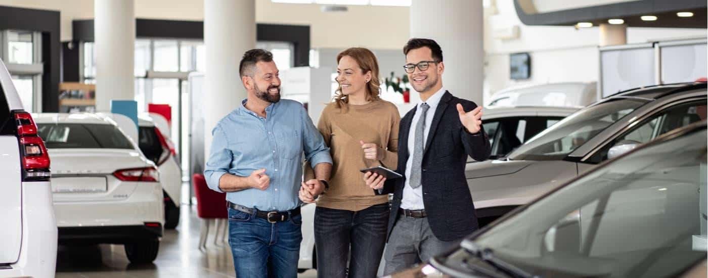 A salesman is speaking to a couple looking for used cars for sale at a dealership.
