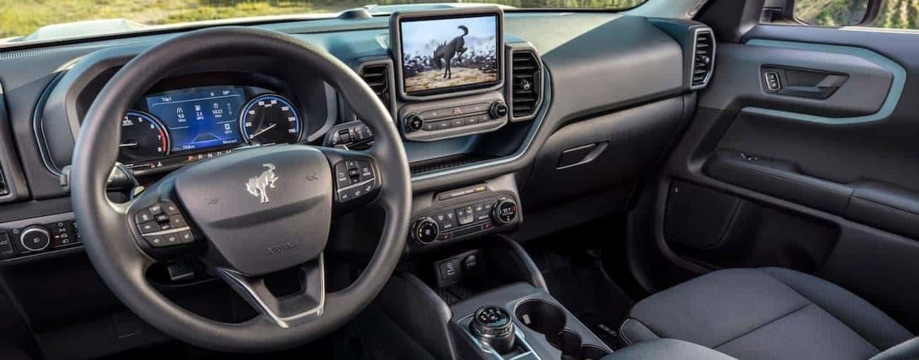 The black interior of a 2021 Ford Bronco Sport shows the steering wheel and infotainment screen.