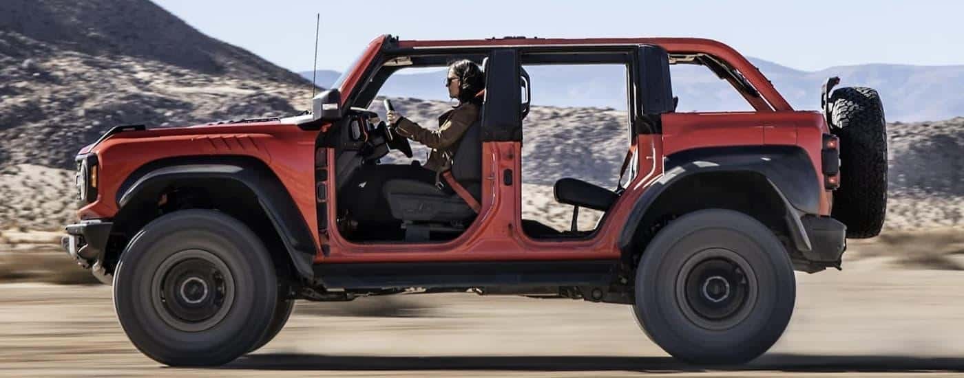 A red 2022 Ford Bronco is shown from the side driving on a dirt road.