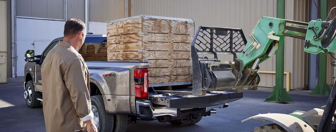 The bed of a silver 2024 Ford F-450 is being loaded with pallets of wood.