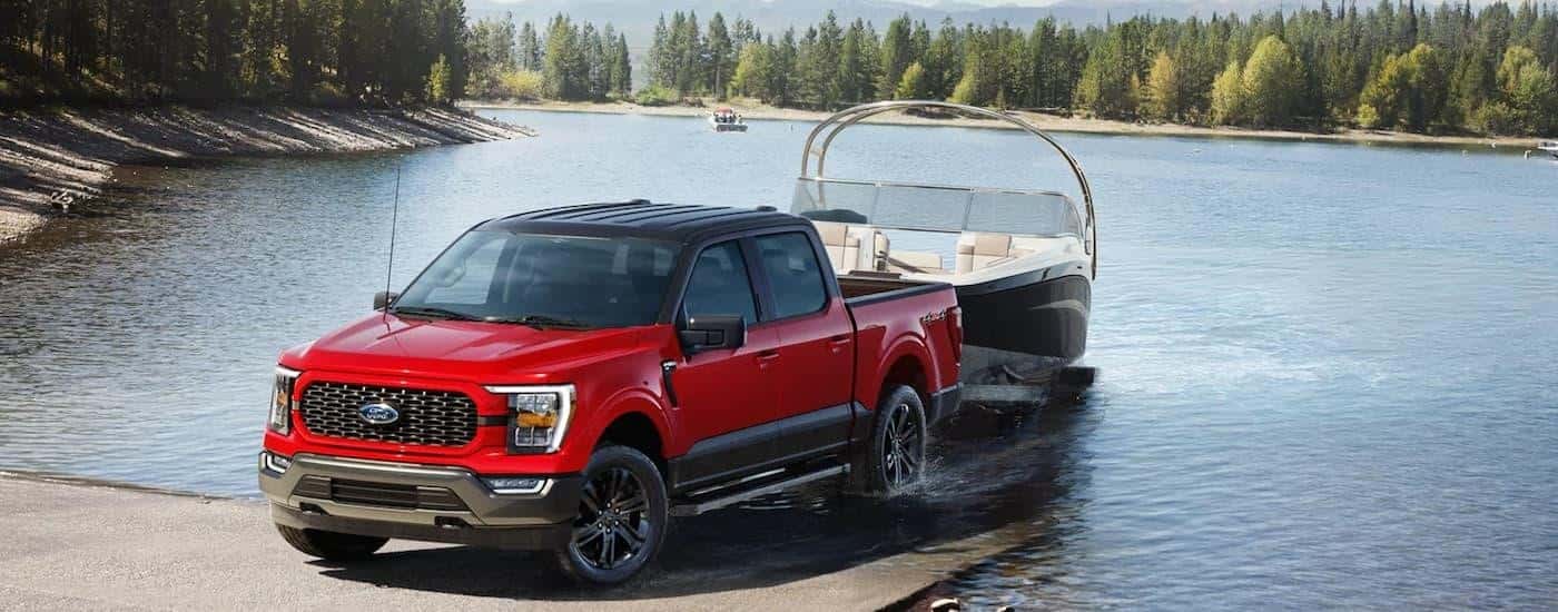 A red 2023 Ford F-150 Heritage is towing a boat out of a lake.