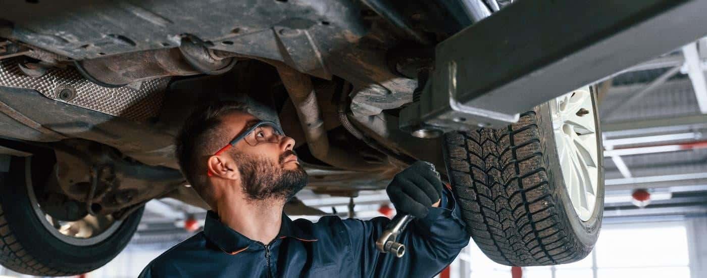 A mechanic is standing underneath a vehicle checking if it needs a strut replacement.
