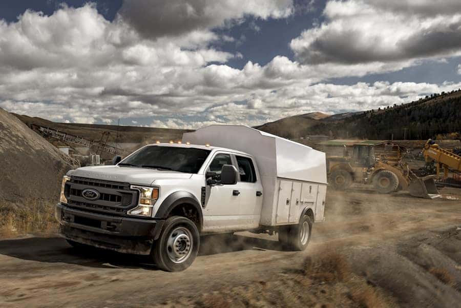 Ford commercial truck with upfit driving up a dirt road.