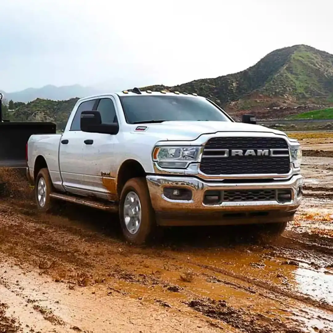 Front 3/4 shot of 2024 RAM 2500 towing heavy machinery through mud.