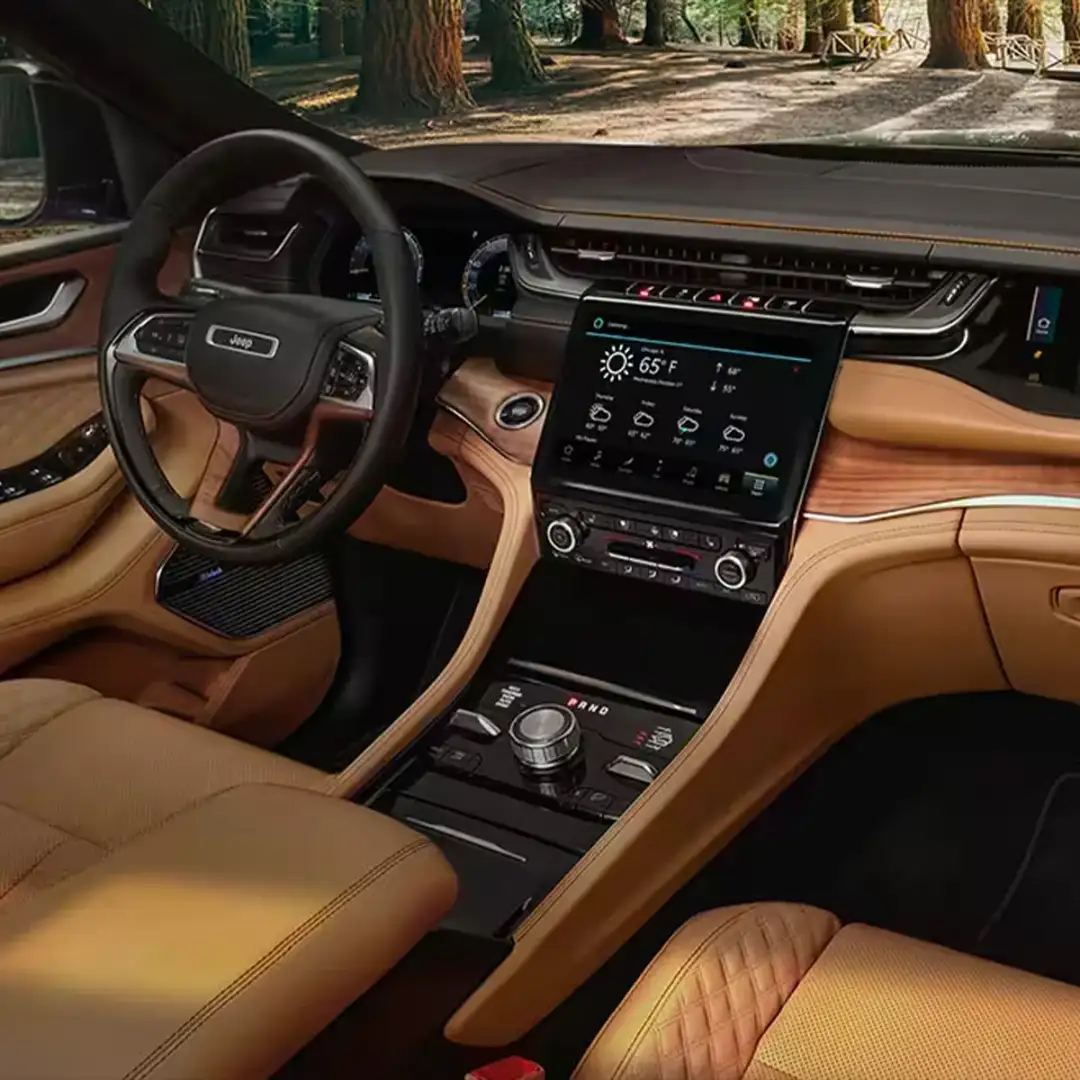 The interior of a 2024 Jeep Grand Cherokee Summit Reserve focusing on the steering wheel, Uconnect touchscreen, center stack and front passenger touchscreen.