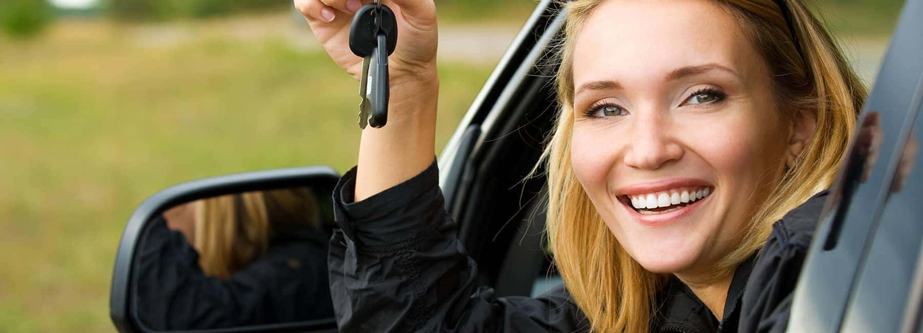 woman leaning out of car smiling with her car keys 