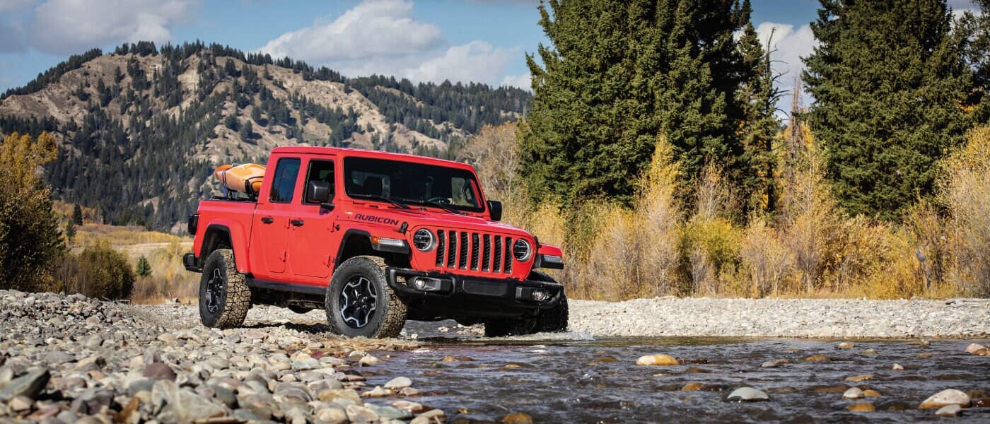 A red 2020 Jeep Gladiator Rubicon off roading in a creek