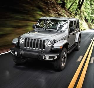 A silver 2019 Jeep Wrangler driving through a woods road