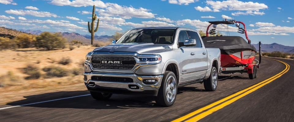 A silver 2019 Ram 1500 towing a boat down an open road