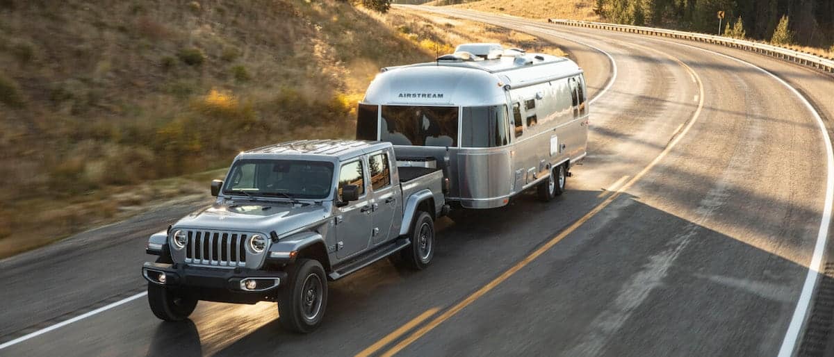 A silver Jeep Gladiator towing a camper on a highway
