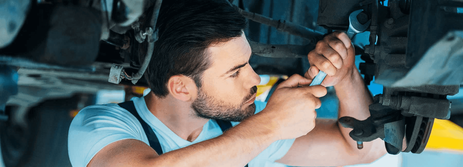 service man with wrench loosens bolt under car
