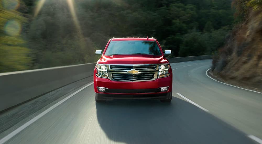 A red 2020 Chevy Tahoe is driving past a corner facing forward on a mountain road.