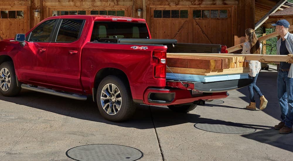 A couple is unloading wood from the bed of a red 2020 Chevy Silverado 1500, which is popular among Chevy trucks, outside a home near Cincinnati, OH.