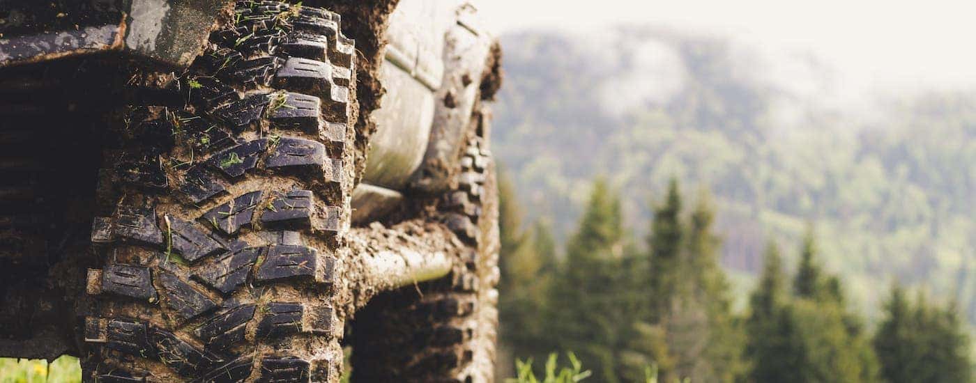 A closeup of a truck's tires is shown covered in mud on a woodland trail.