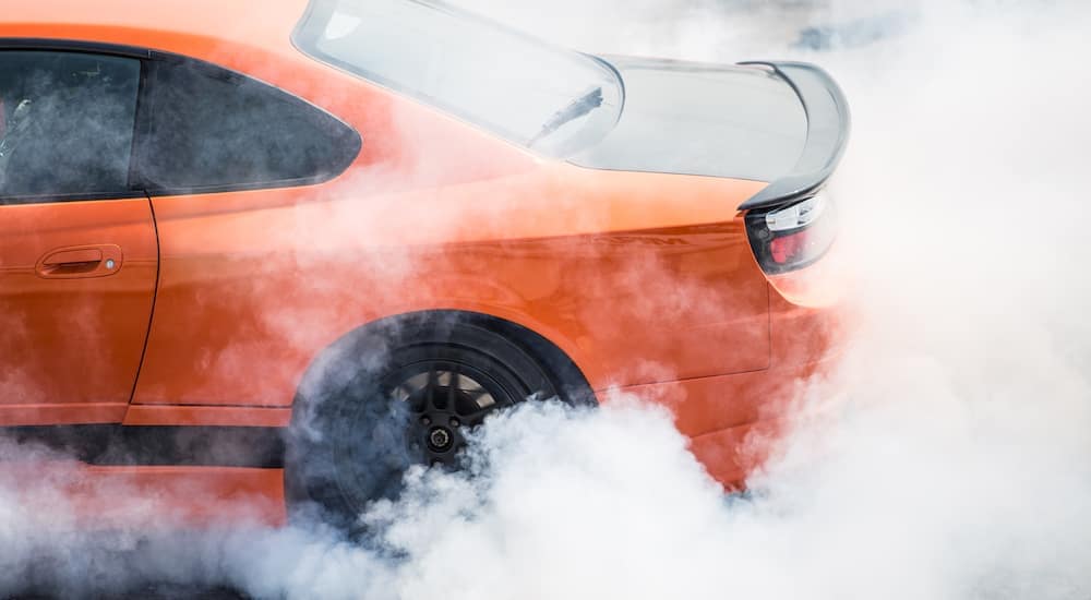 An orange car is doing a burnout and kicking up smoke.
