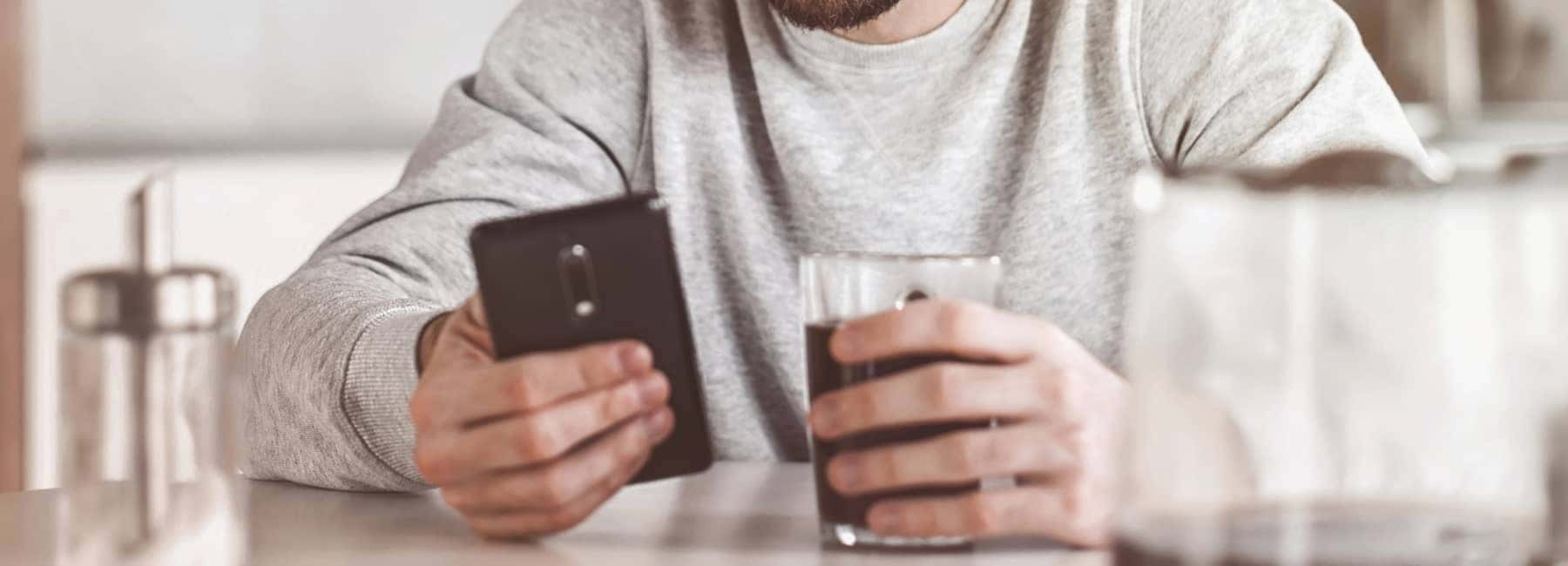 A person with a glass of coffee looking at their phone