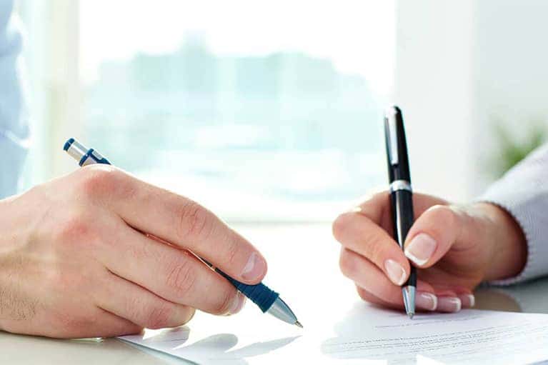Two Hands Holding Pens Signing a Document