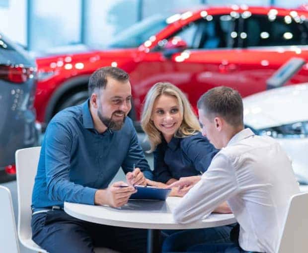 Two people in a dealership showroom sitting with a finance advisor