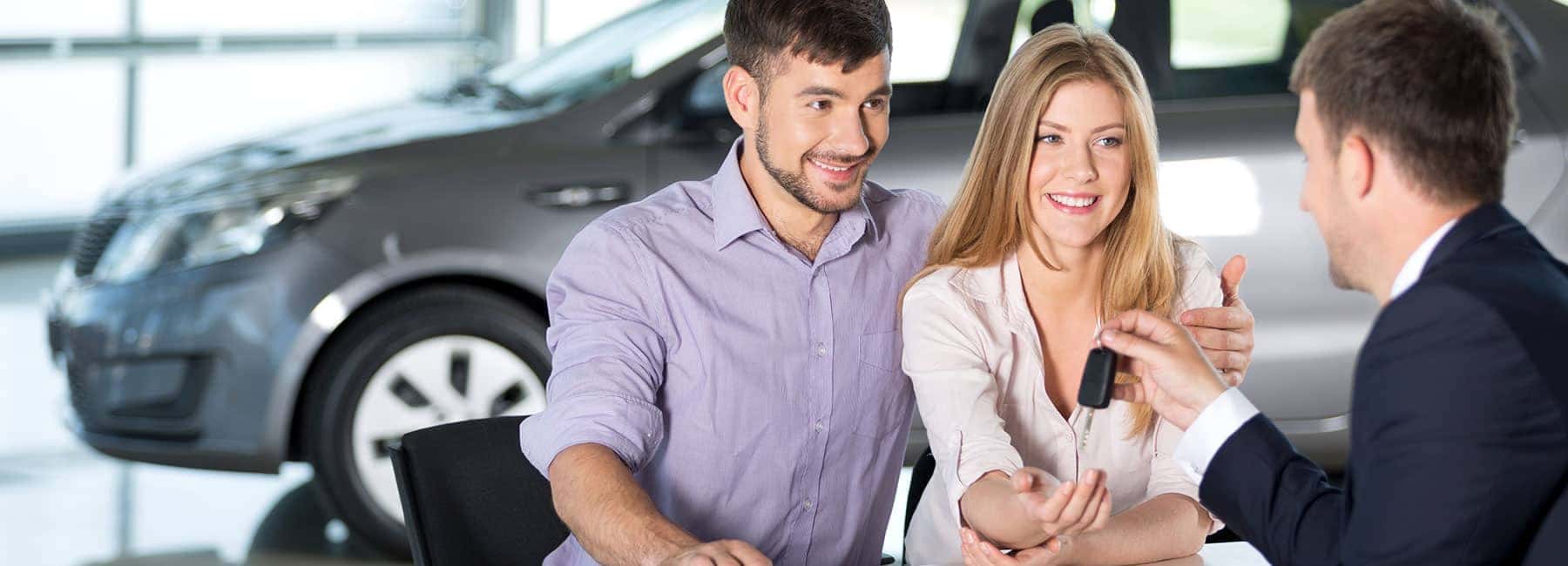 Salesman Handing Car Key to a Young Couple in Showroom
