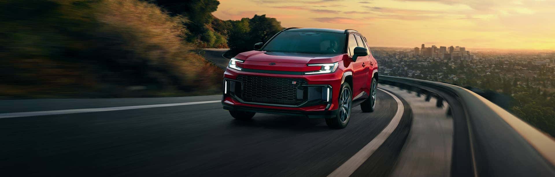 Red Toyota SUV driving winding mountain road at sunset